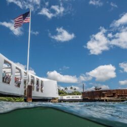 A scenic view of the USS Arizona Memorial with a clear blue sky and American flag.