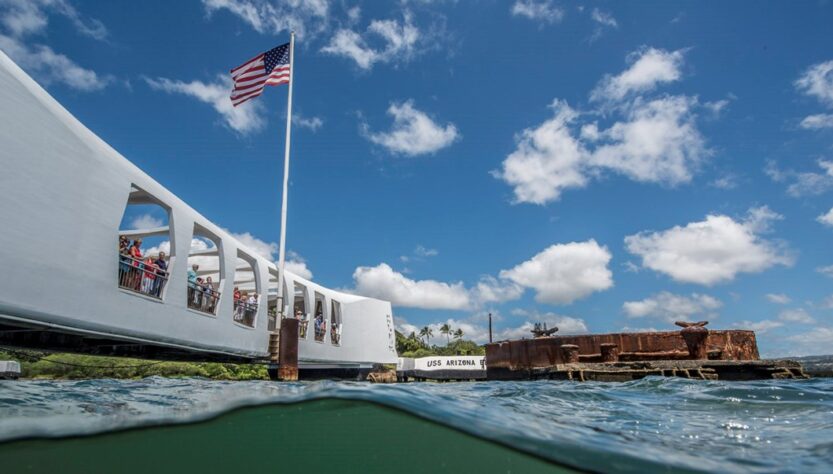 A scenic view of the USS Arizona Memorial with a clear blue sky and American flag.